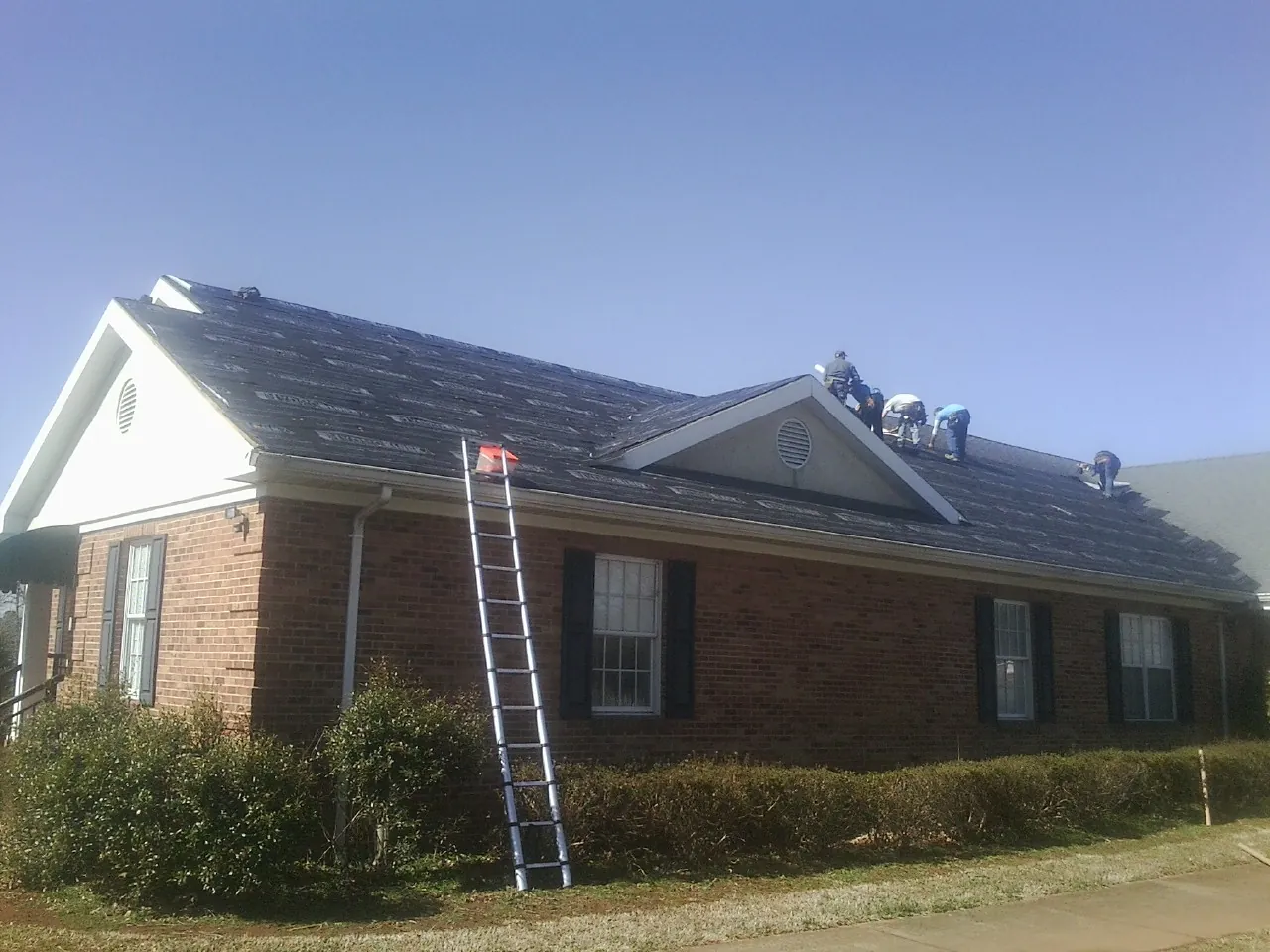 Crew tearing shingles off a brick ranch roof with a ladder set — Emergency Roof Repair work by our crew in Frenchglen