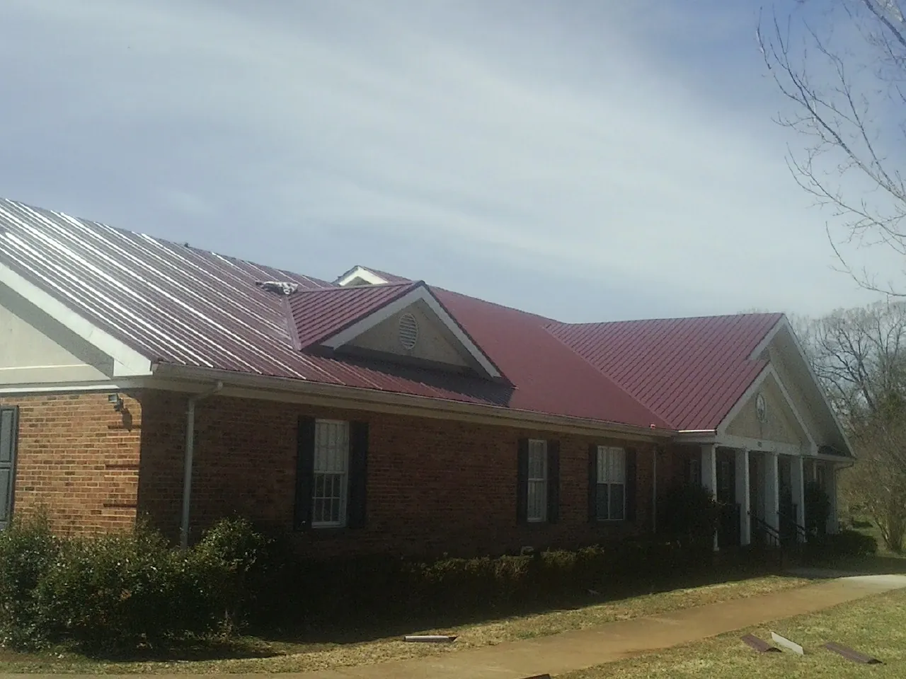Red metal roof with gabled entries on a long brick building, from a Hail Damage Roof Repair job in Frenchglen