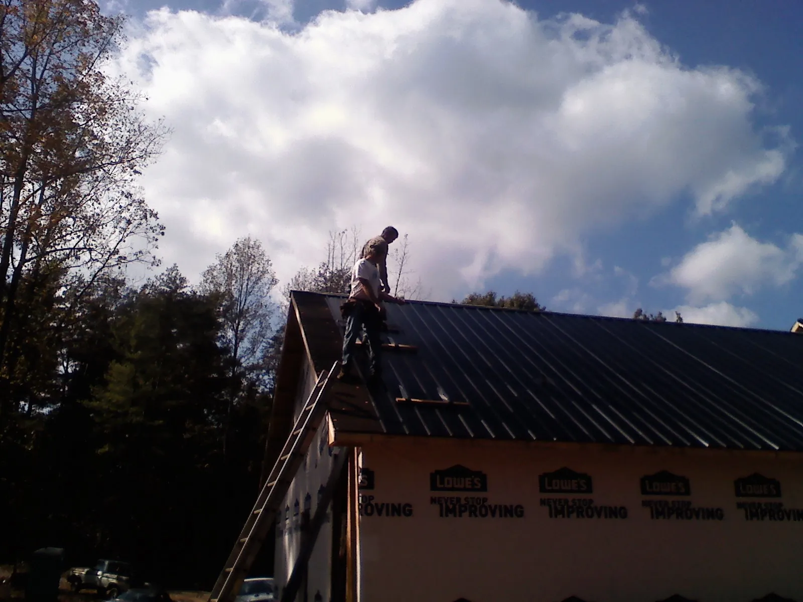 Roofer fastening dark metal panels high against a cloudy sky, from a Roof Inspection job in Frenchglen