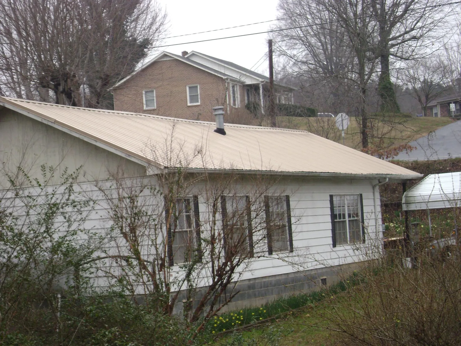 Tan metal roof on a white sided house set into a hillside — Commercial Roofing by Roofing Brothers in Frenchglen